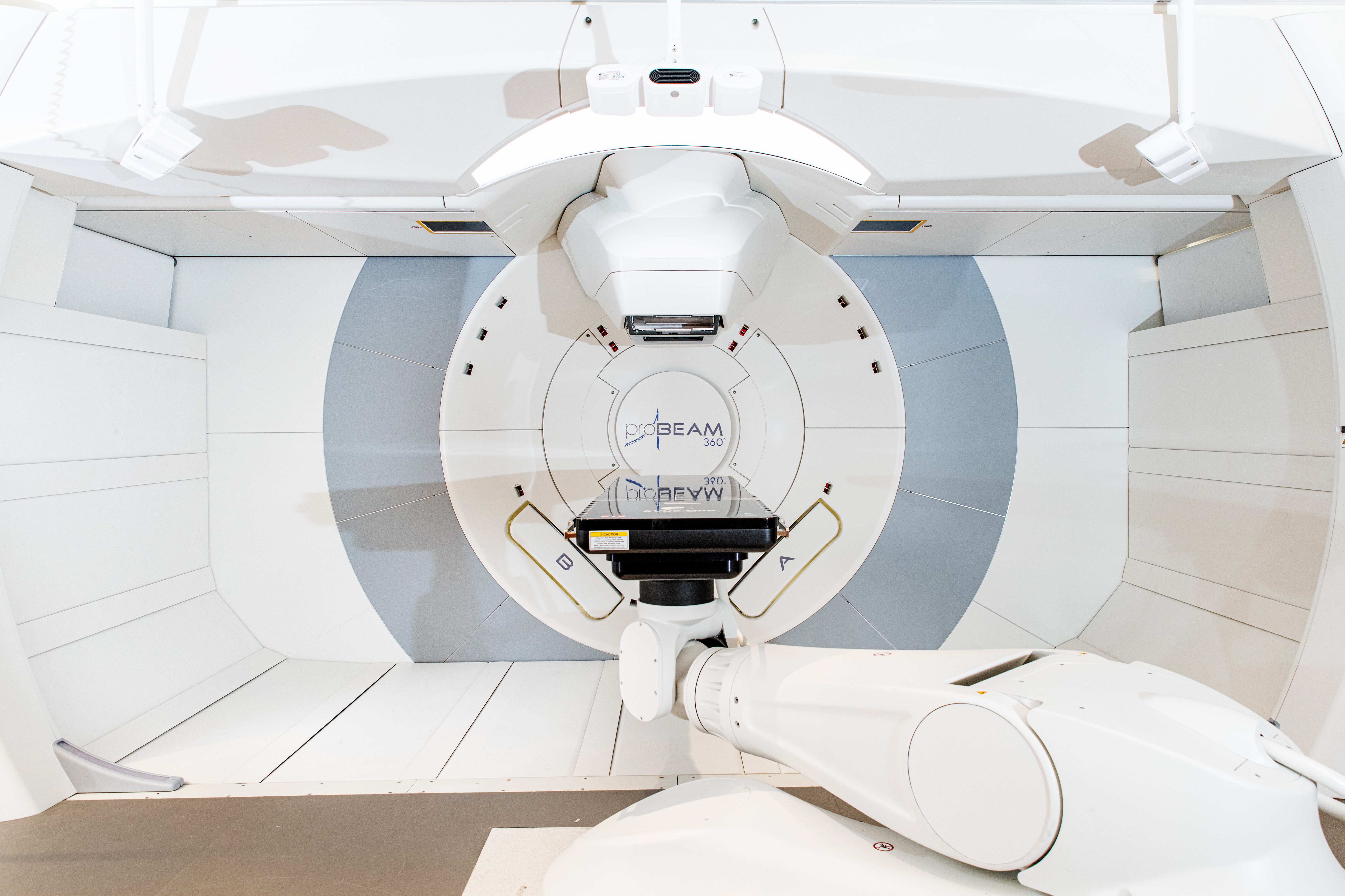 Hvit maskin i en slags trommel, med plater over og under. Beam i skrift på veggen bak. Foto.