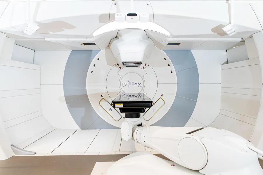 Hvit maskin i en slags trommel, med plater over og under. Beam i skrift på veggen bak. Foto.