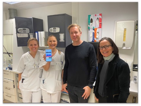 En gruppe mennesker som poserer for et bilde. To i sykehusklær. Viser en skjerm på telefon.