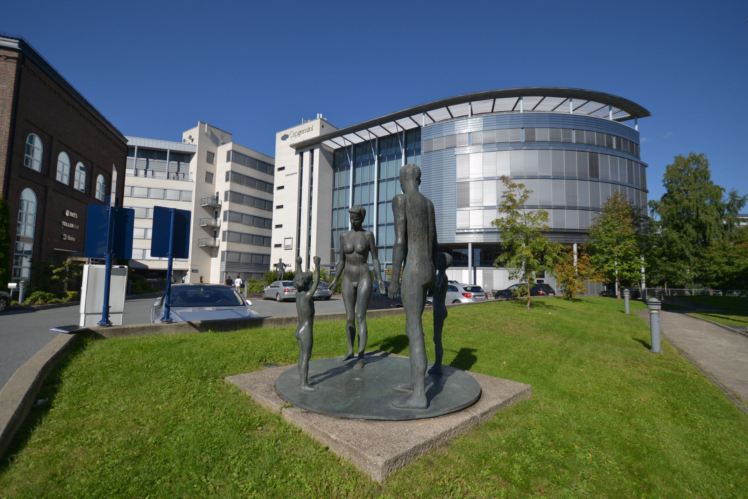 Kontorbygg i glass og mur. Statue og gress foran. Foto.