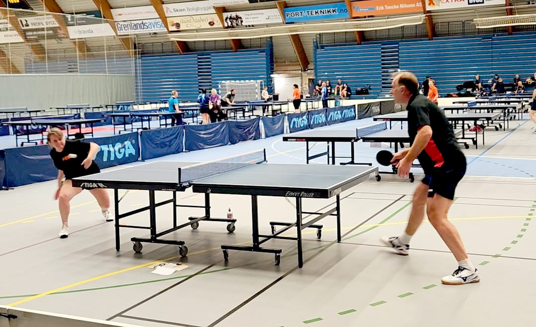 Et par personer som spiller bordtennis i en stor innendørs arena
