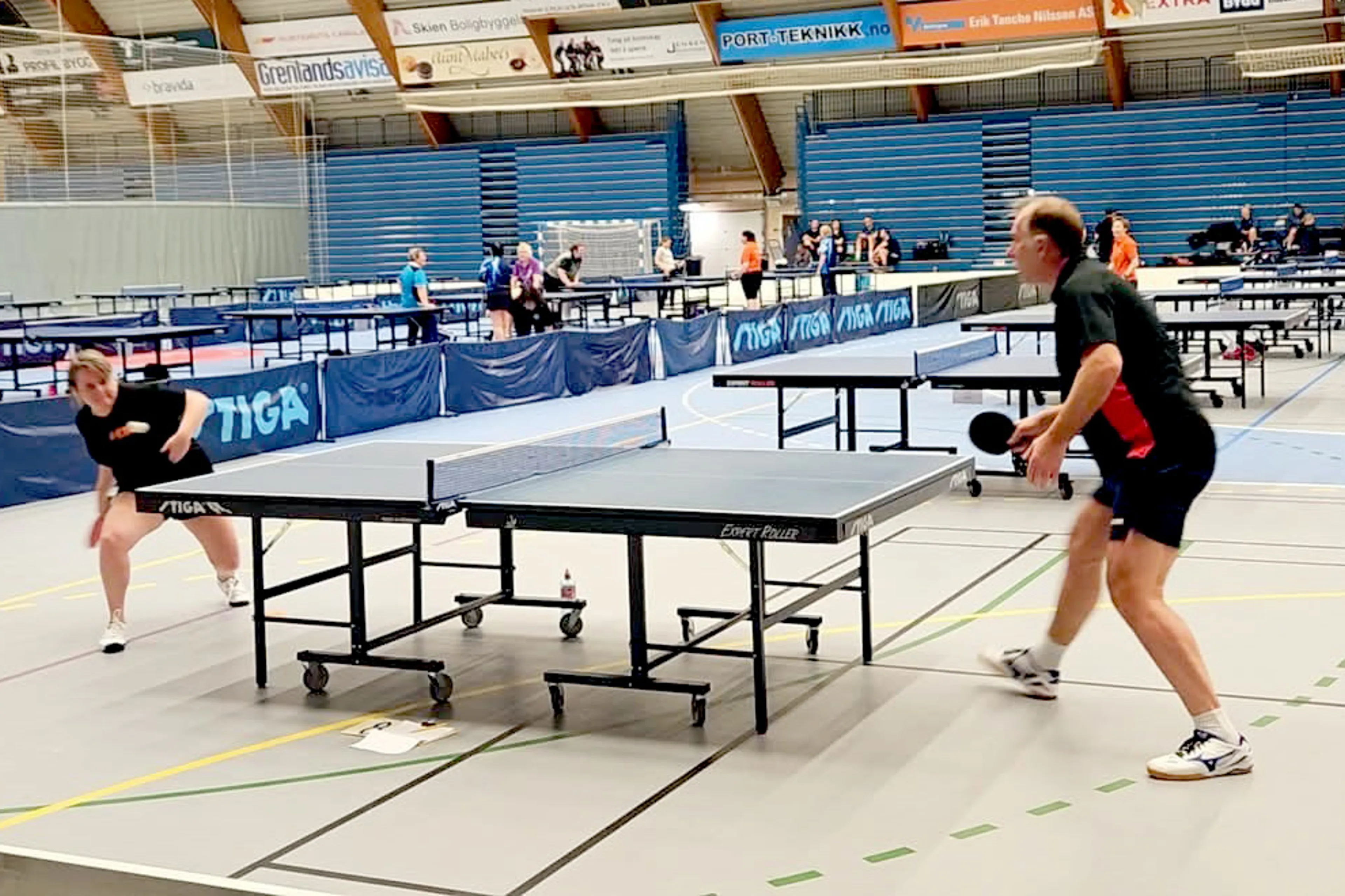 Et par personer som spiller bordtennis i en stor innendørs arena