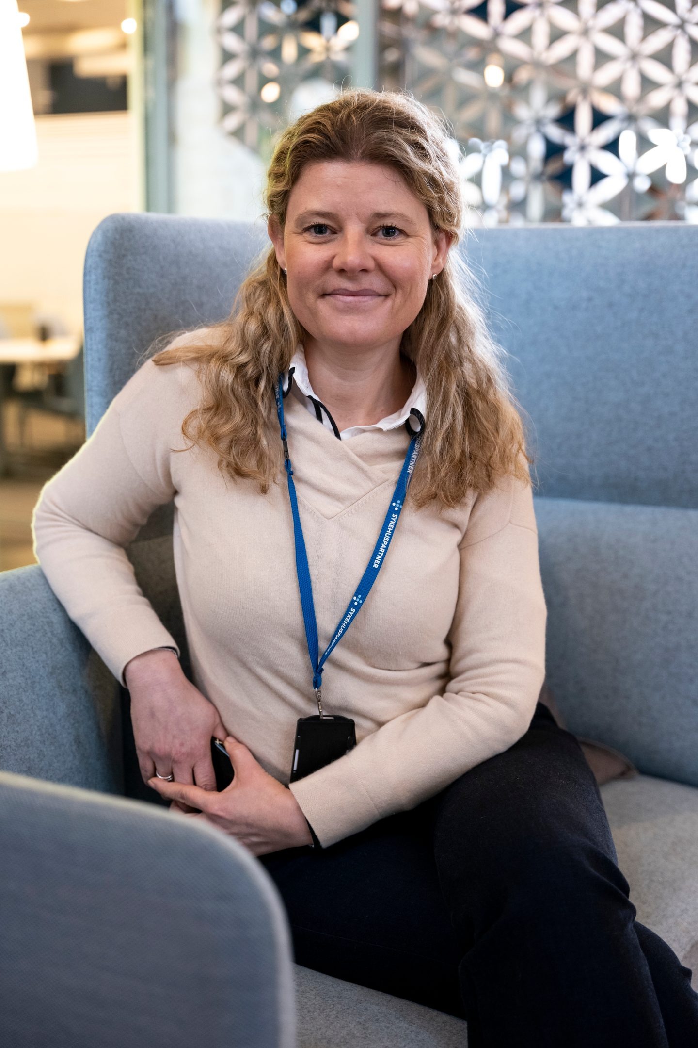 En kvinne med langt blondt hår, som sitter i en stol. Foto.