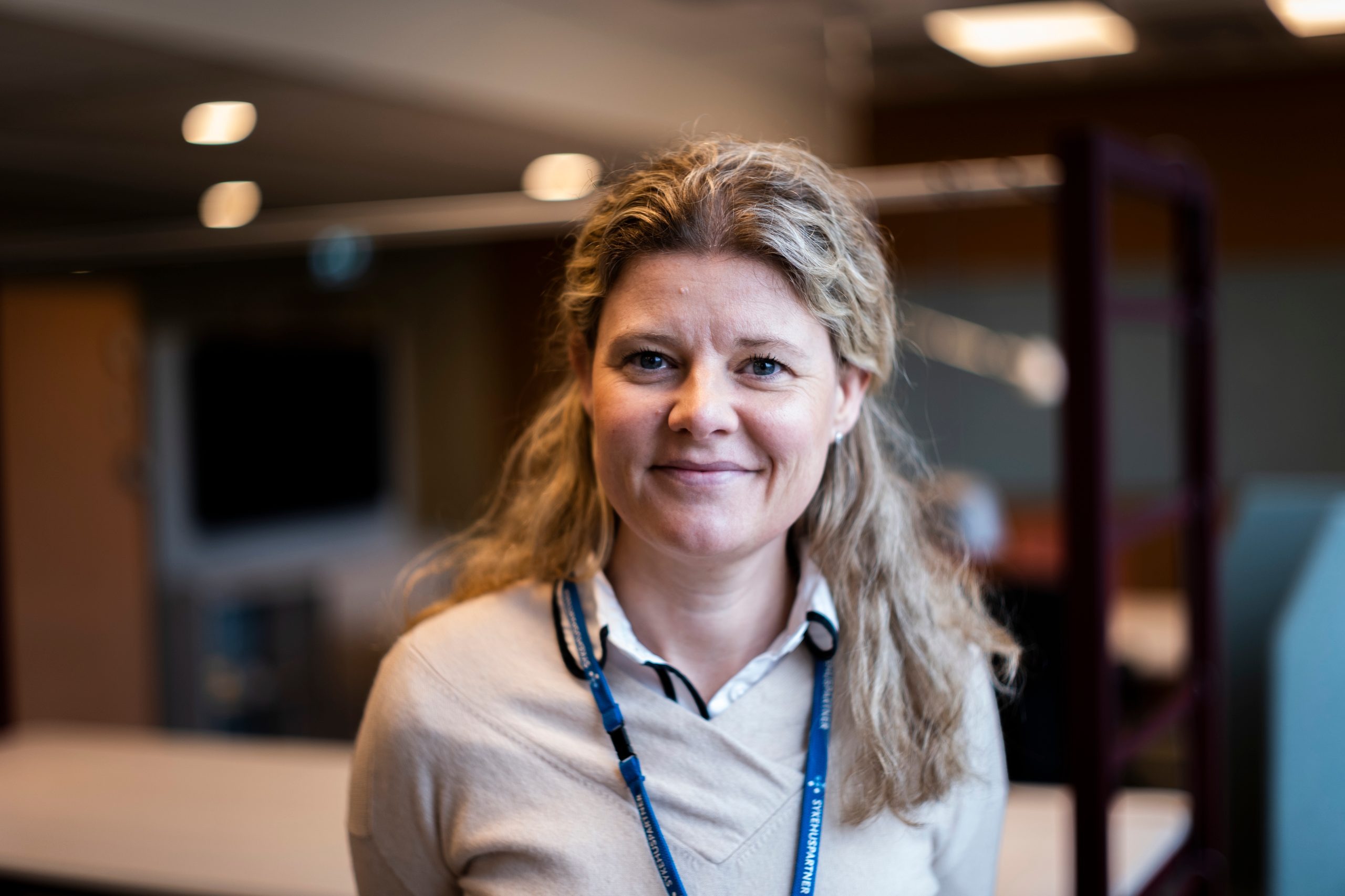 Smilende kvinne med langt, blondt hår. Foto.