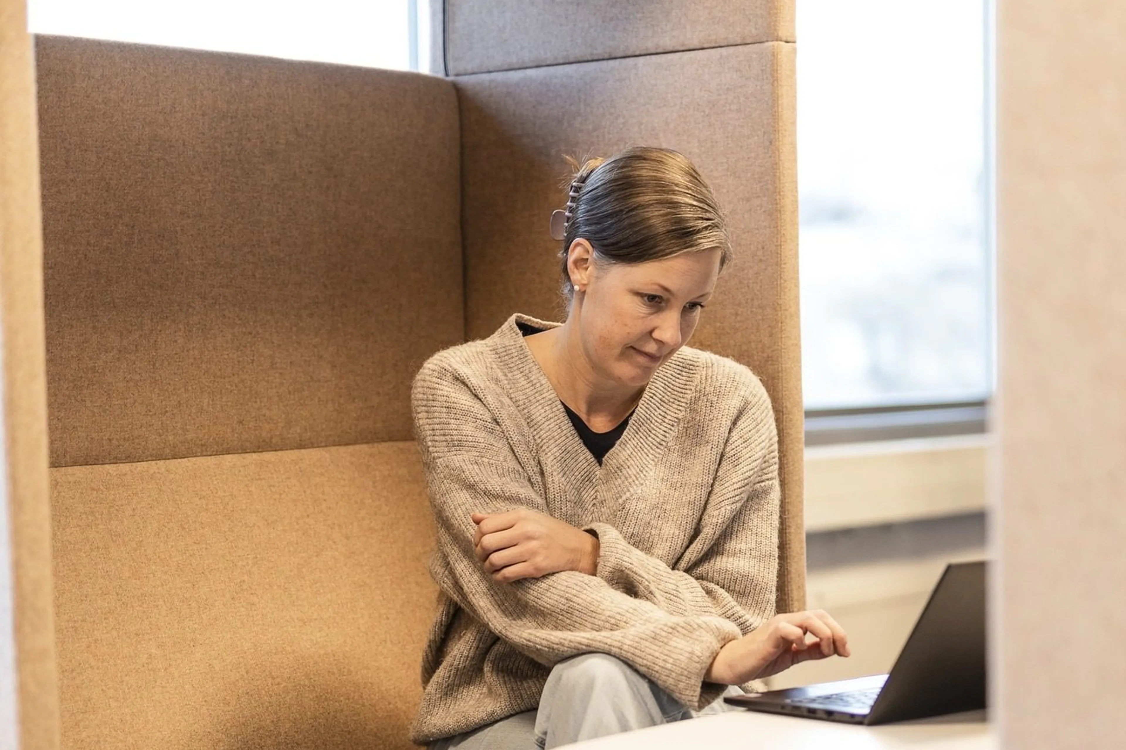 En kvinne som sitter på et kontor, ser på en PC-skjerm. Foto.