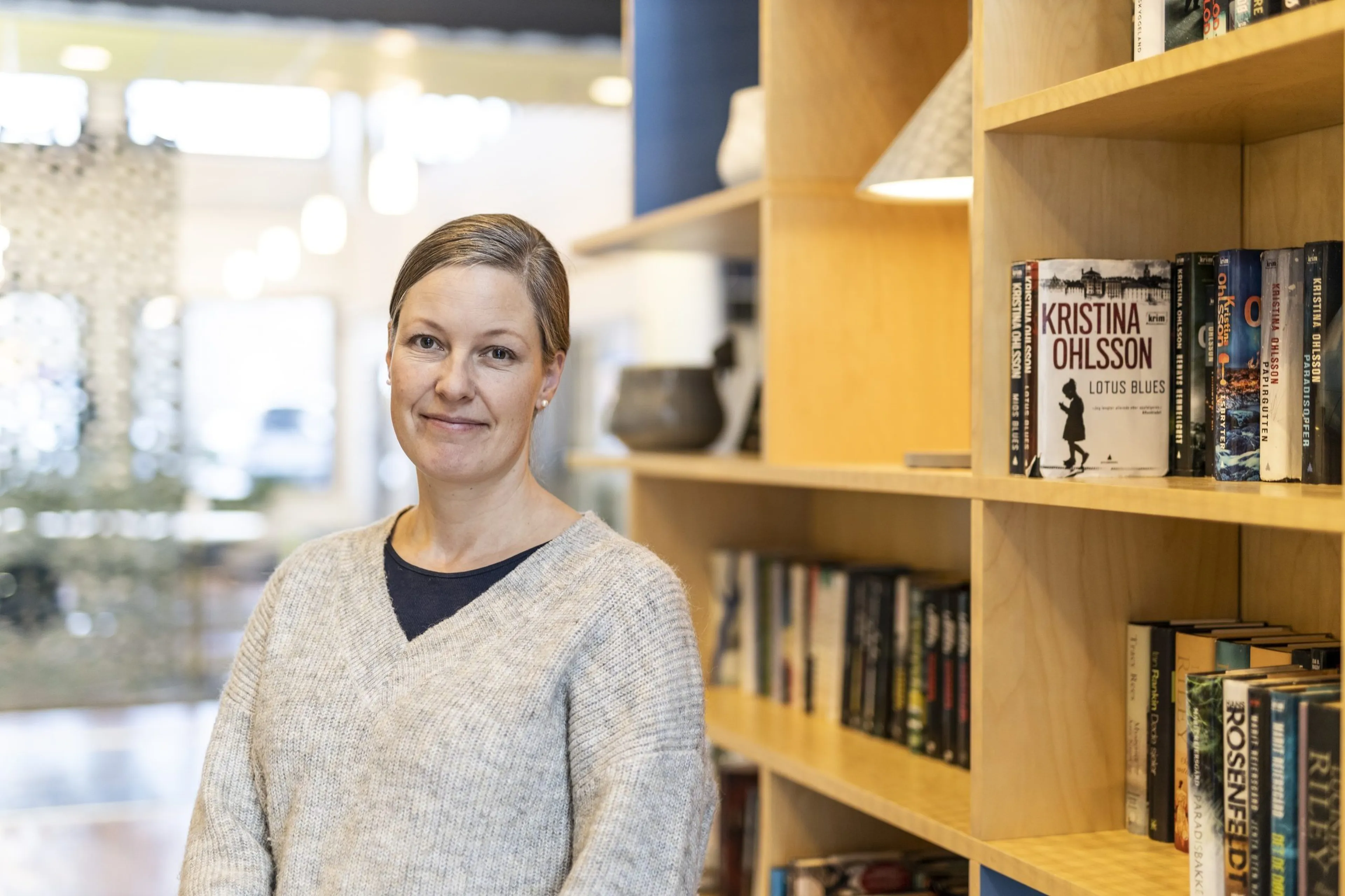 Smilende kvinne som står foran en bokhylle. Foto.
