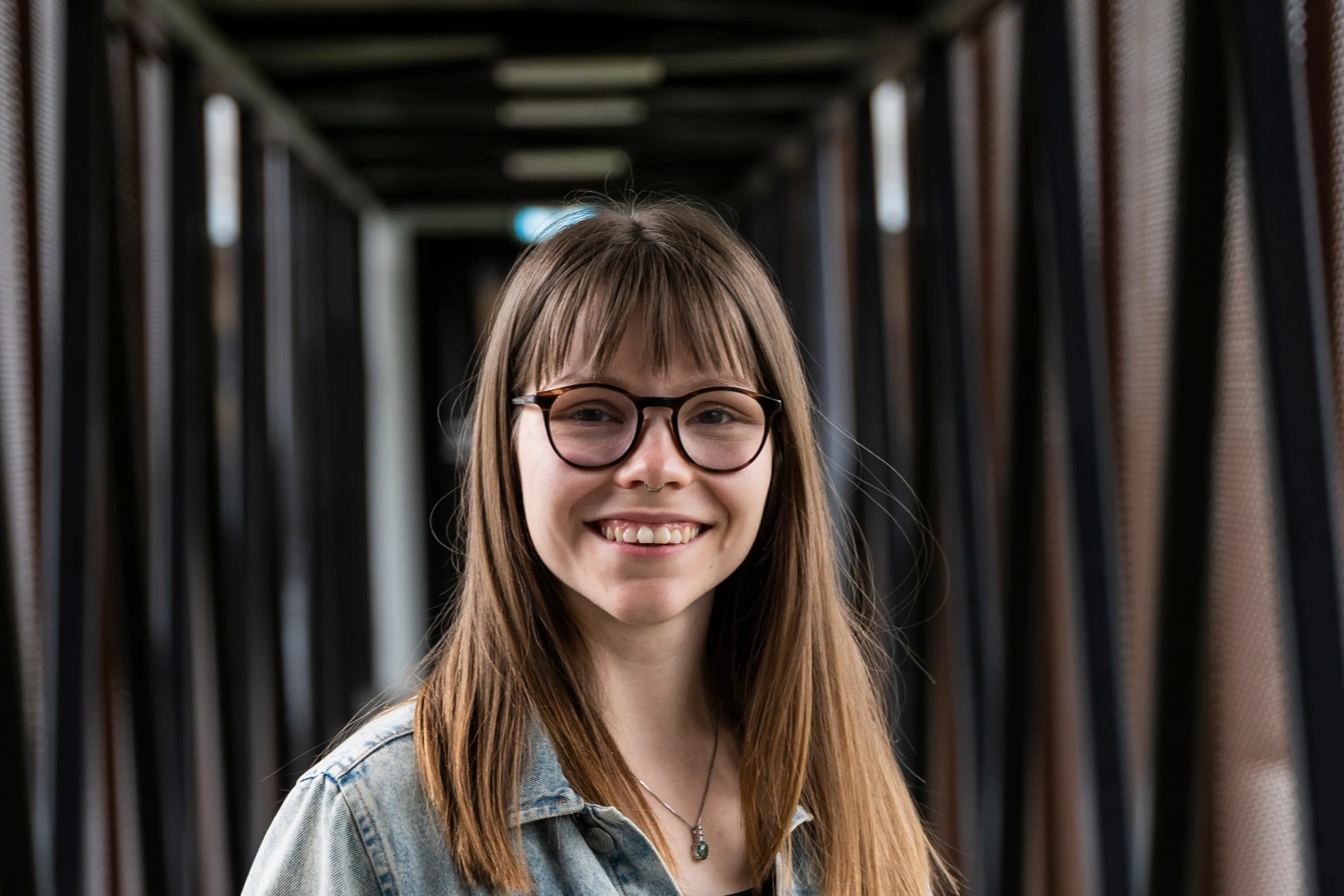 Smilende kvinne med langt, brunt hår og briller. Foto.