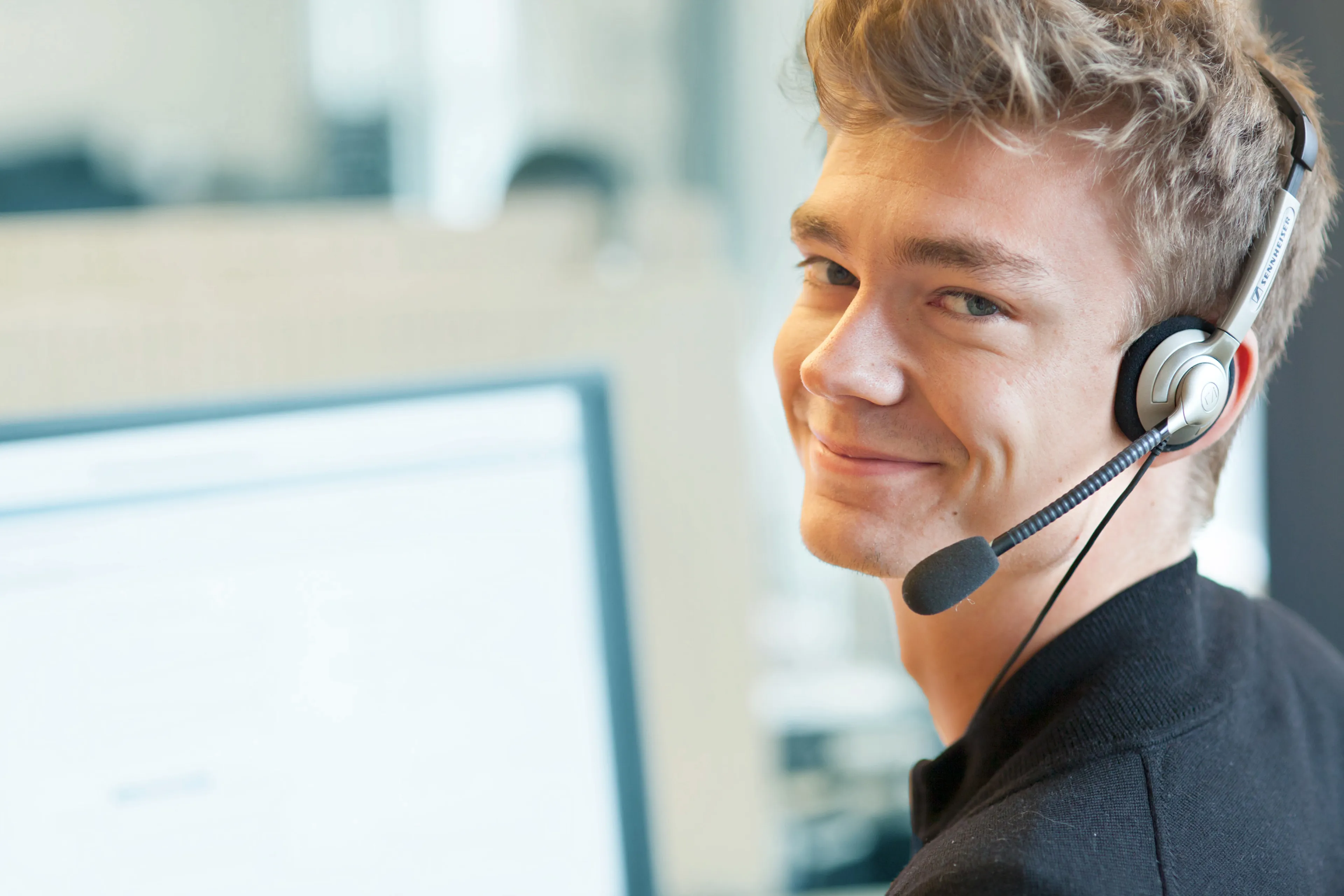 A man wearing phone headphones, in front of a computer.