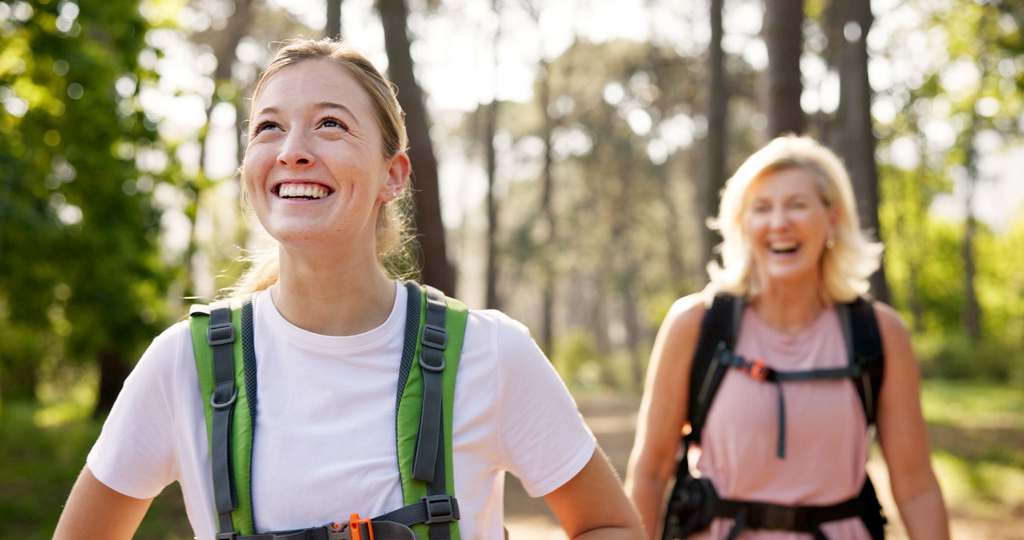 A couple of women smiling, hiking in the woods.