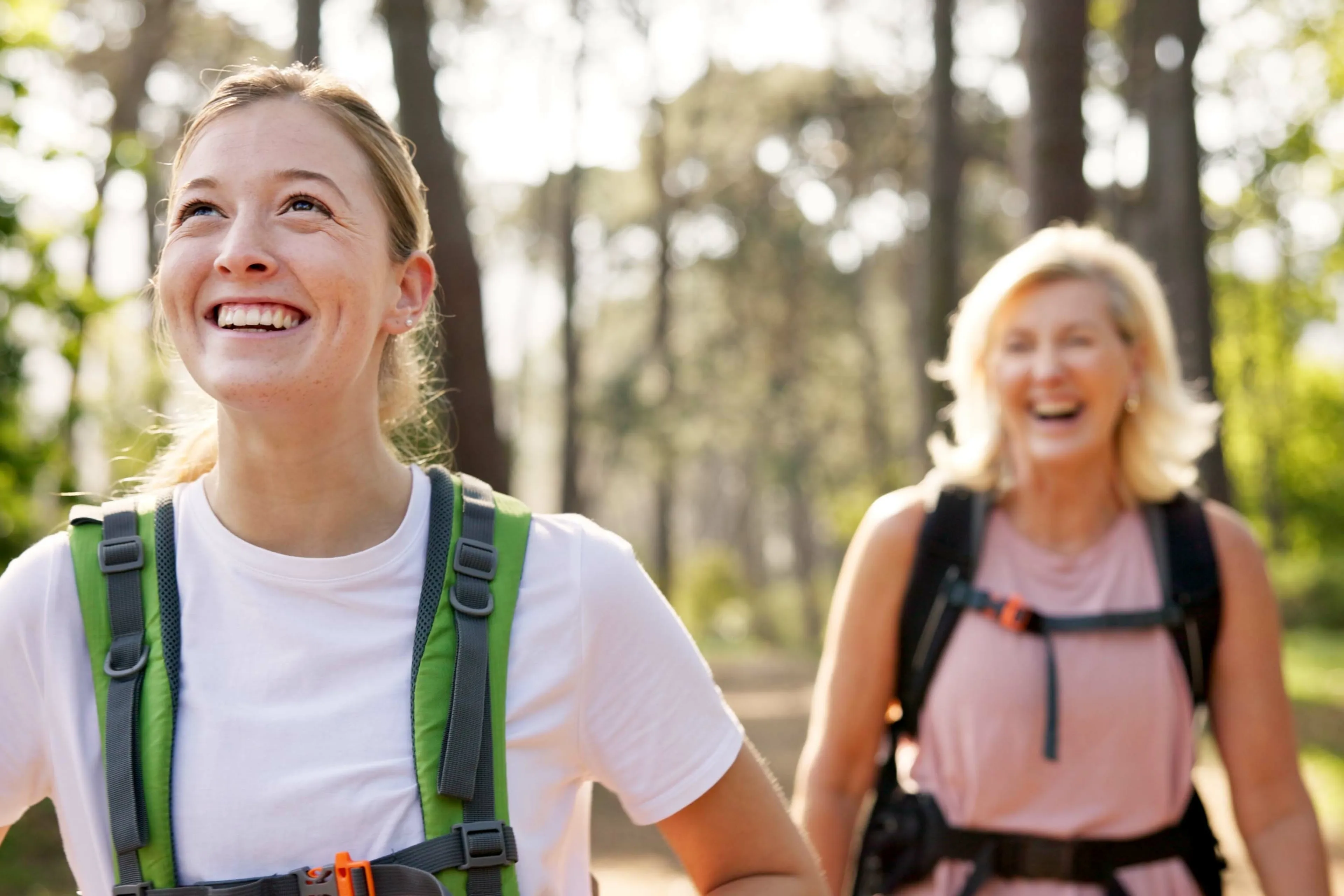 A couple of women smiling, hiking in the woods.