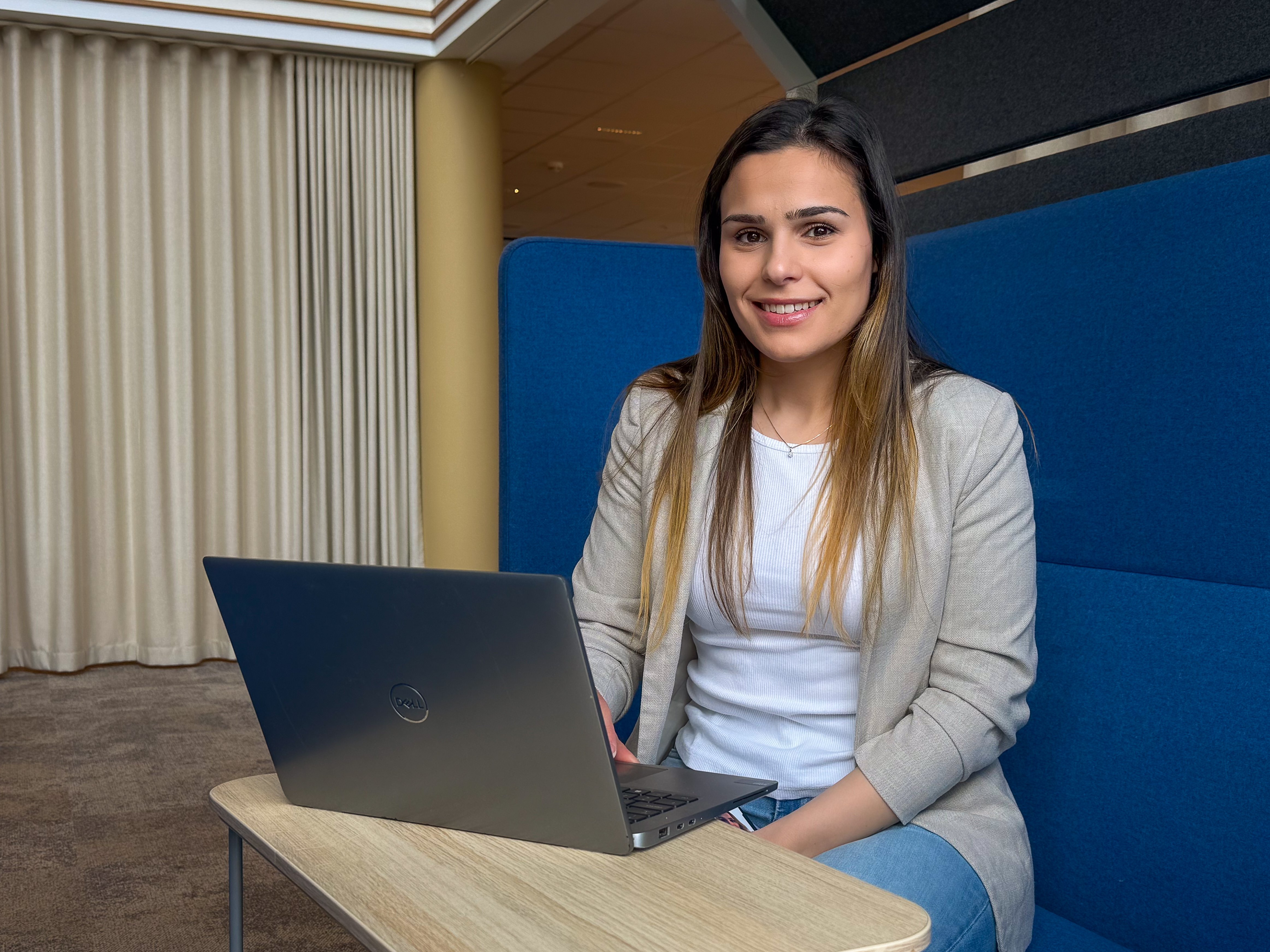 Smilende kvinne med langt hår som sitter bak en pc