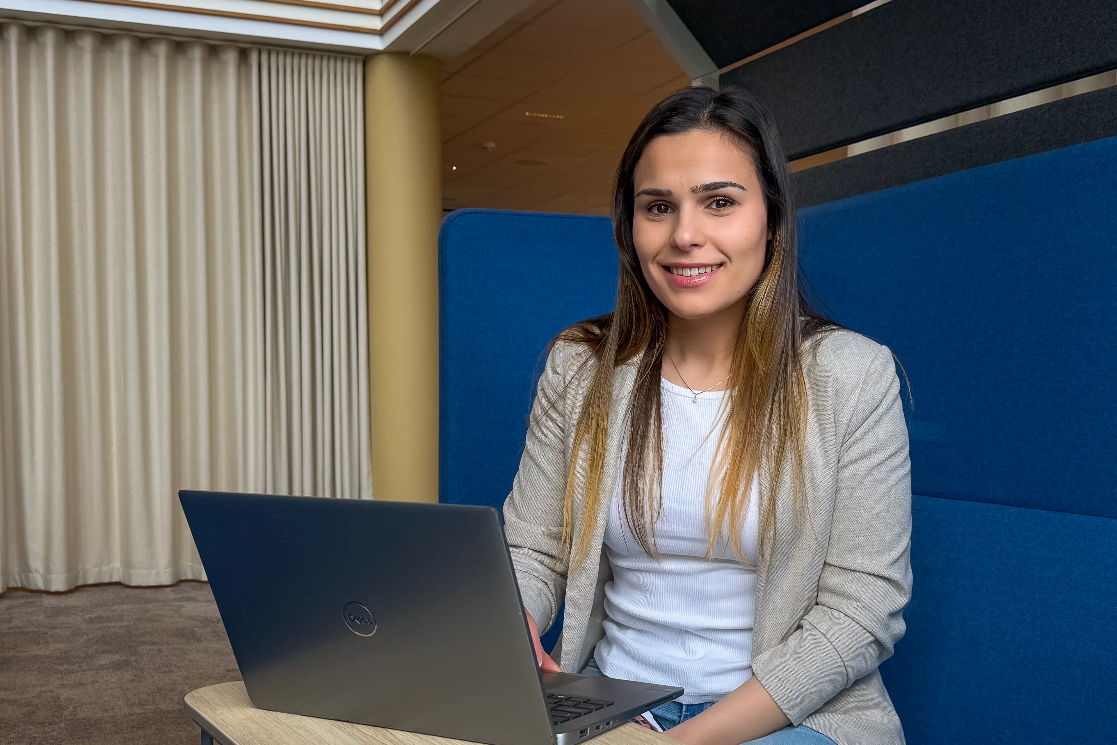 Smilende kvinne med langt hår som sitter bak en pc