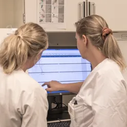 To damer i hvit frakk som ser på en pc-skjerm.