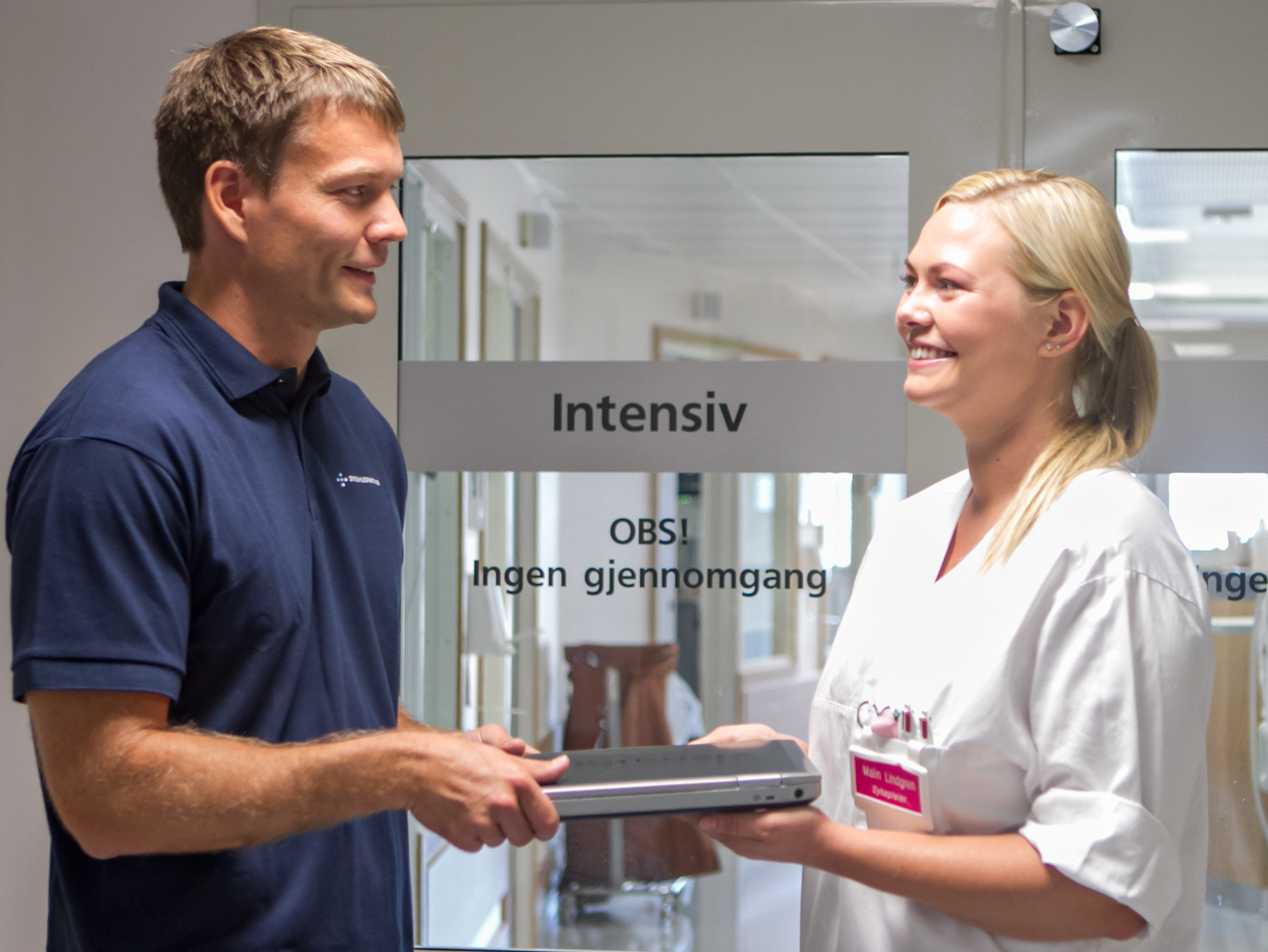 Mann og som overrekker en bærbar pc til en kvinnelig sykehusansatt som smiler