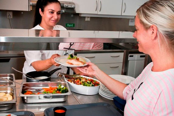 En person som tar imot en tallerken med mat fra kjøkkenpersonell