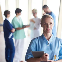 Kvinnelig doktor med ipad, helsepersonell diskuterert i bakgrunnen