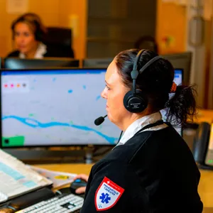 Dame ansatt i prehospitale tjenester med headset foran 2 skjermer