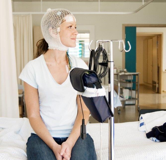 Pasient som sitter på seng med elektroder på hodet