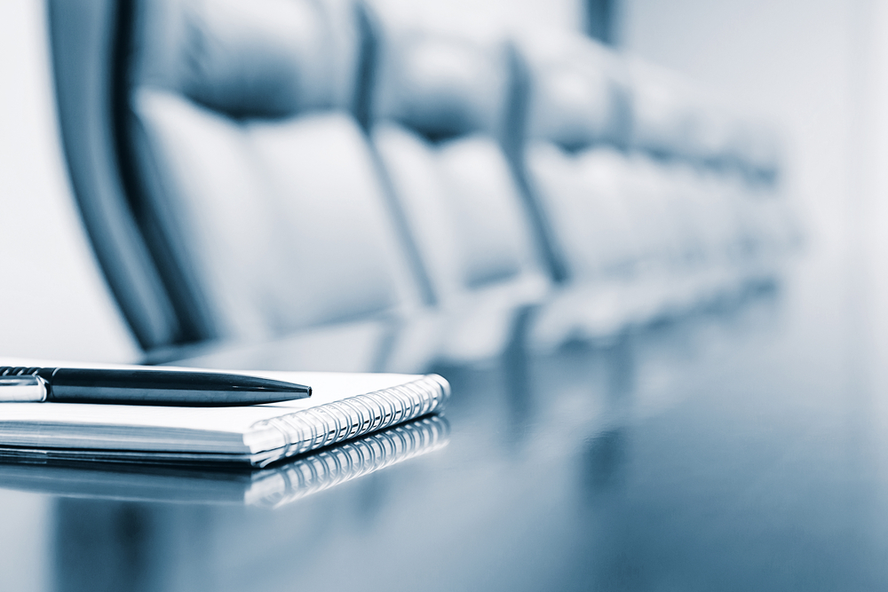 Skriveblokk på bord med mange stoler rundt. Foto.