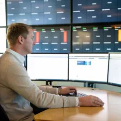 En mann som sitter ved et skrivebord med flere skjermer