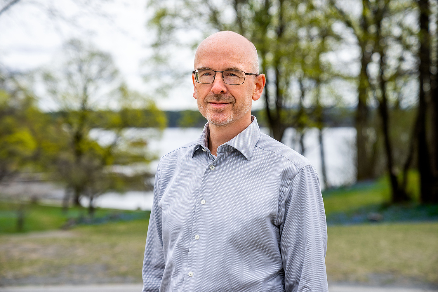 Smilende mann med briller og lyseblå skjorte. Foto.