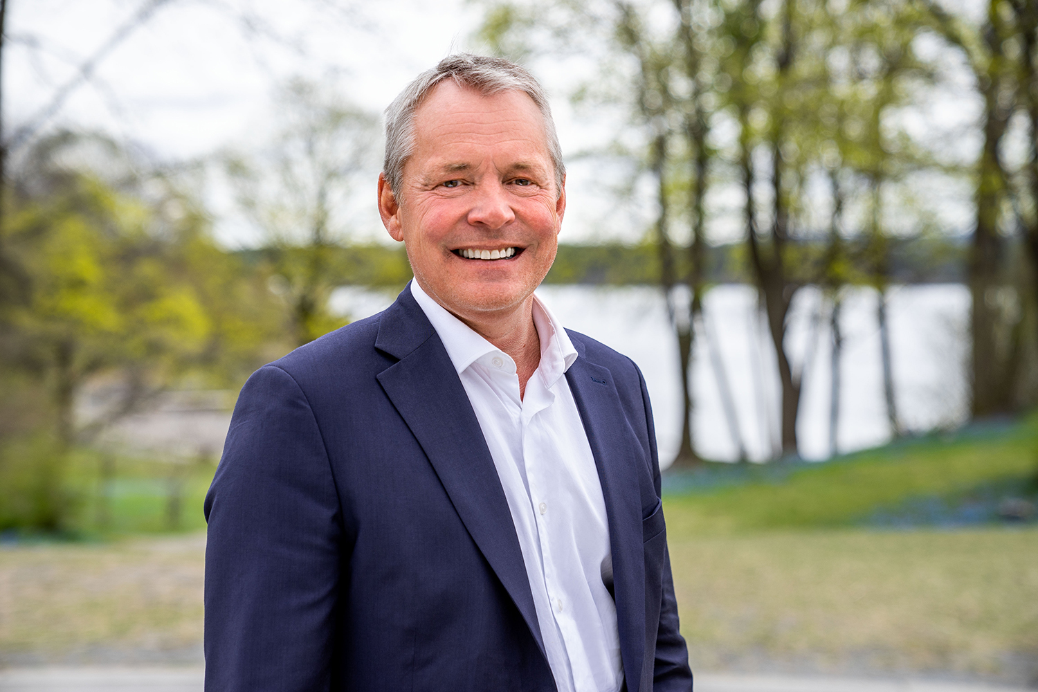 Smilende mann med grått hår, skjorte og dressjakke. Foto.