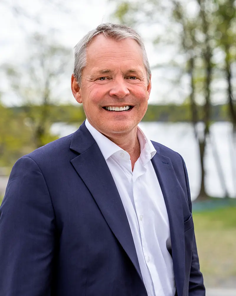 Smilende mann med grått hår, skjorte og dressjakke. Foto.