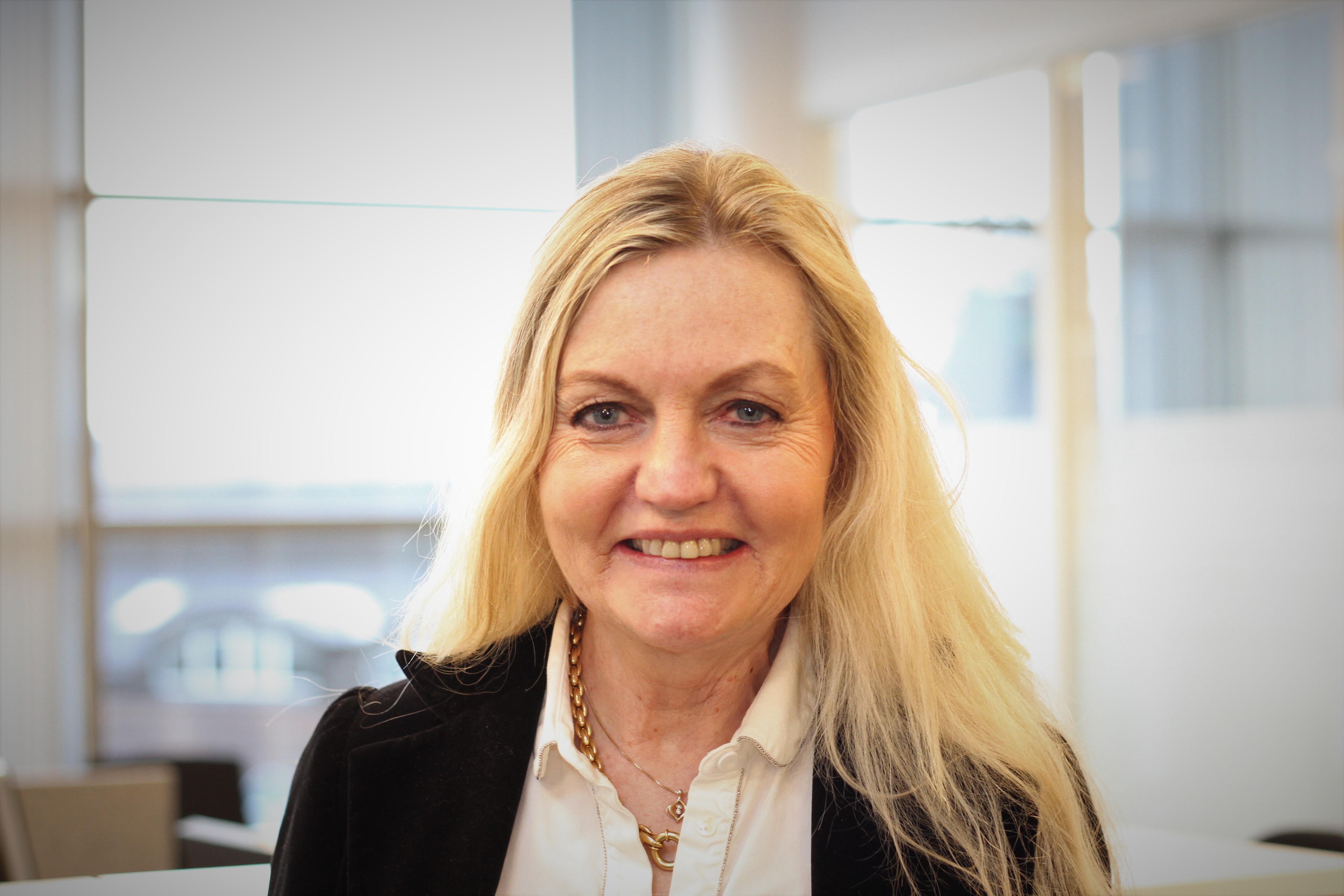 Smilende dame med langt, blondt hår. Foto.