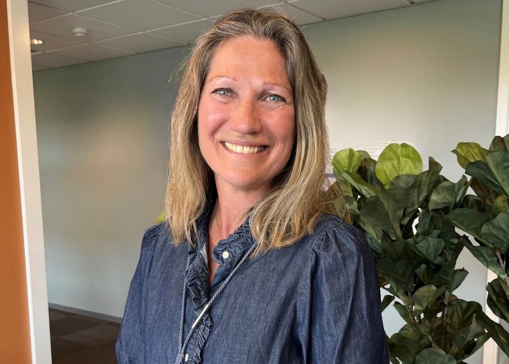 Smilende kvinne med mellomlangt, blondt hår. Foto.