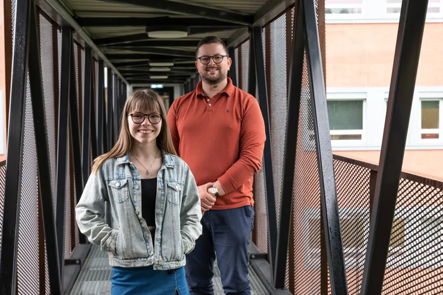 En mann og kvinne, begge med briller, står ved siden av hverandre og smiler. Foto.