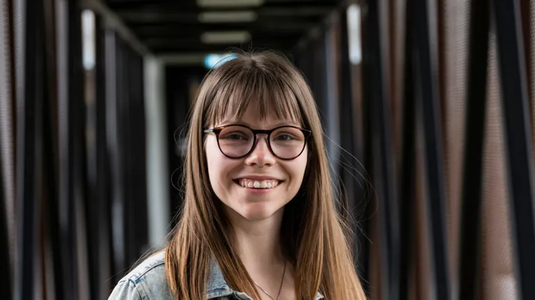 Smilende kvinne med langt, brunt hår og briller. Foto.