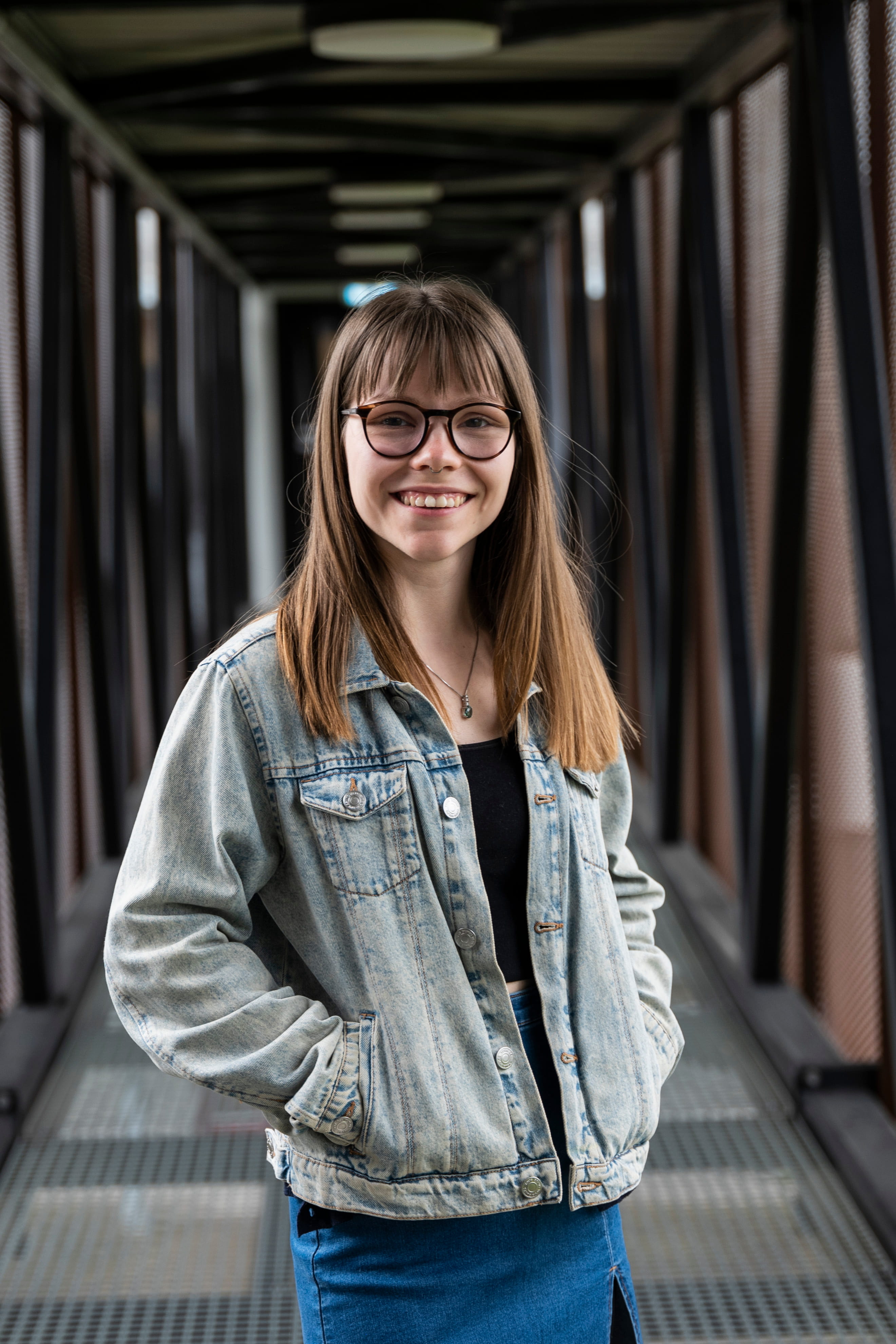 Smilende kvinne med langt, brunt hår og briller. Foto.