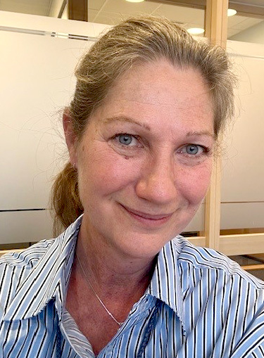 Smilende kvinne med grått, langt hår i hestehale. Foto.