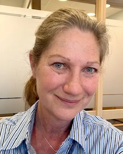 Smilende kvinne med grått, langt hår i hestehale. Foto.