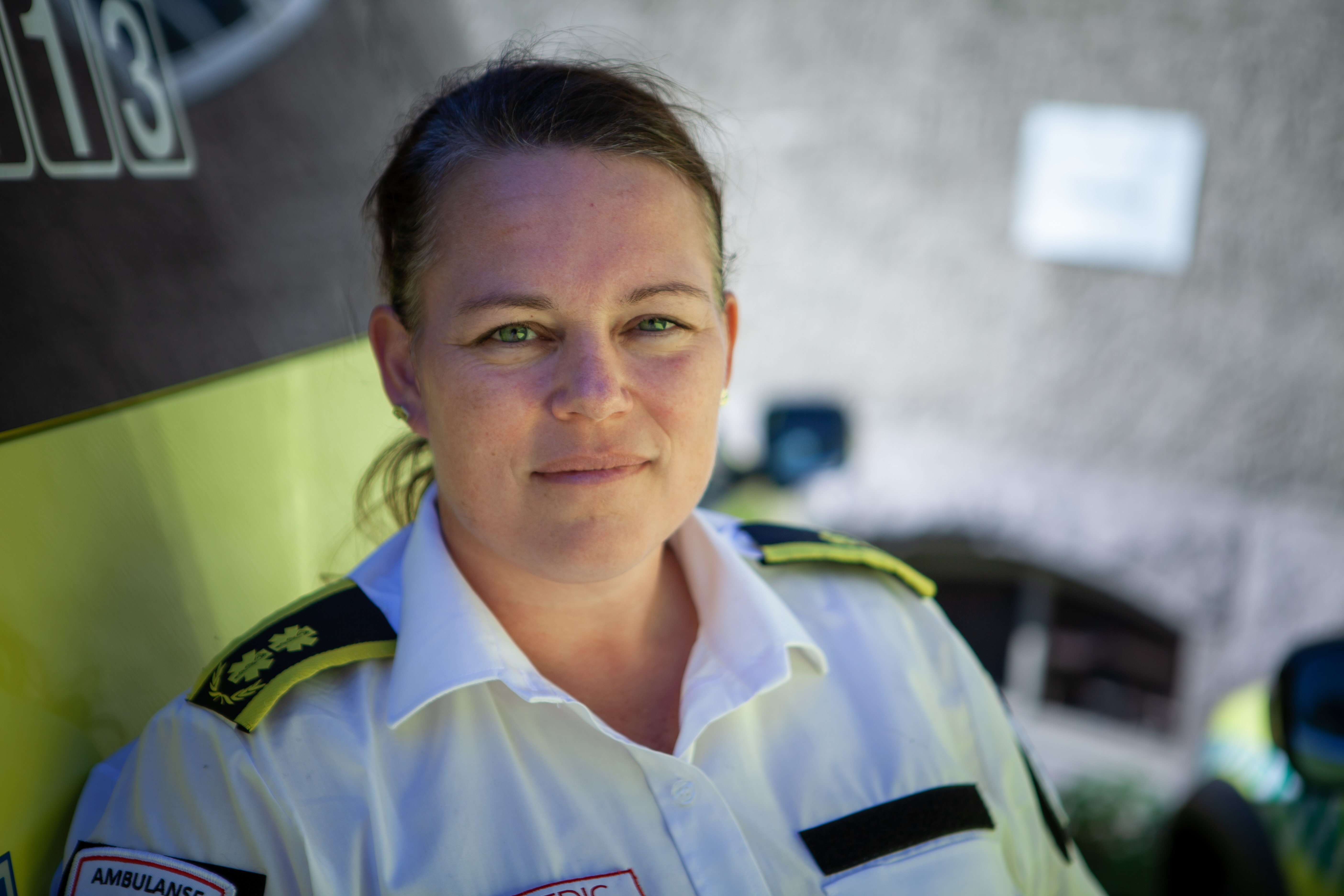 Kvinne i hvit skjorte med ambulansemerker. Foto.