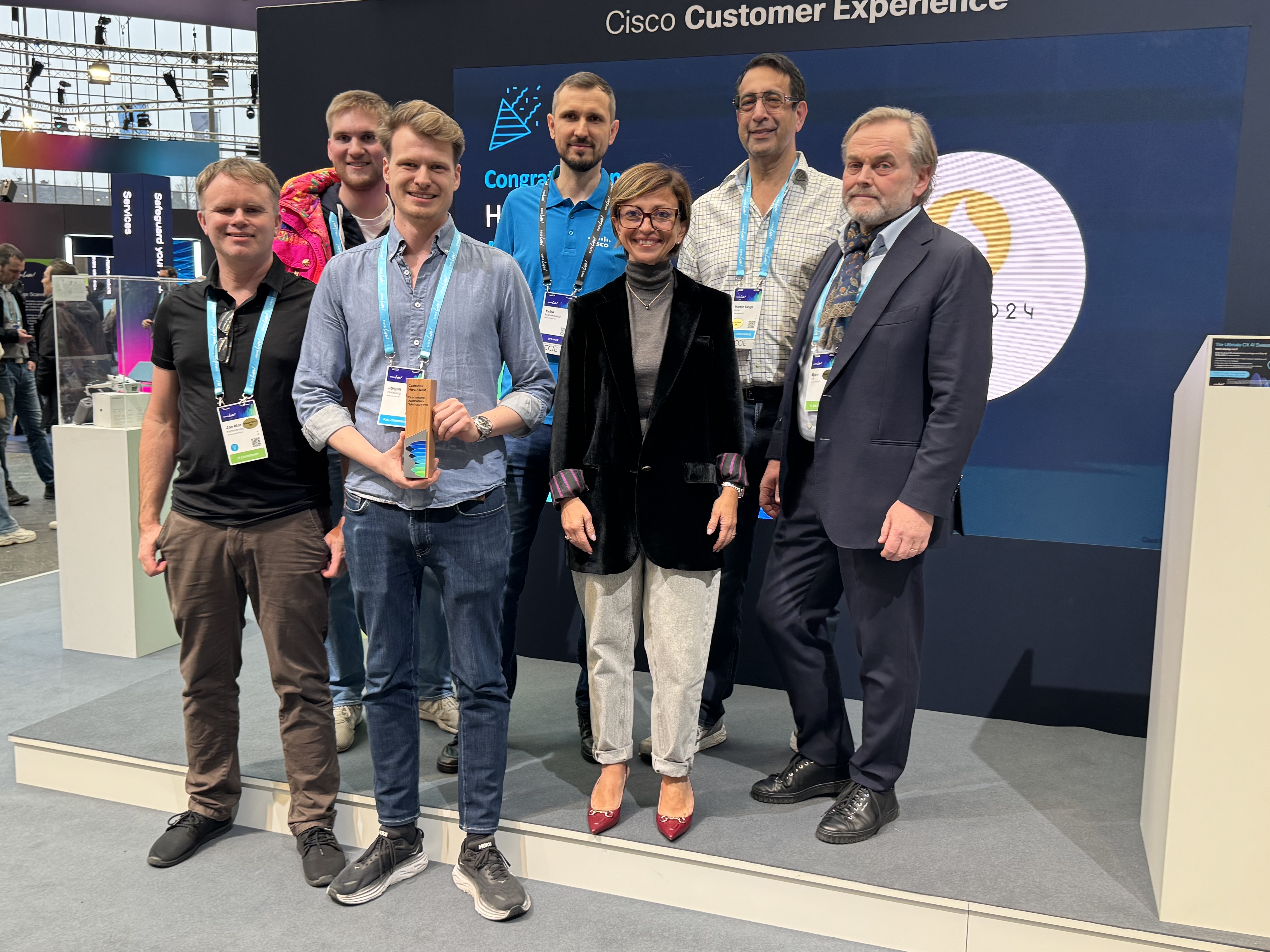 En gruppe smilende mennesker som poserer for et bilde i en messehall. En holder en premie. Foto.