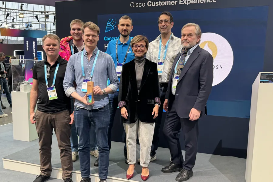 En gruppe smilende mennesker som poserer for et bilde i en messehall. En holder en premie. Foto.