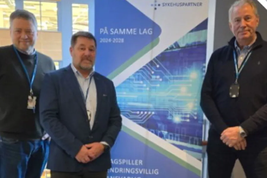 Tre menn som står foran en plakat med Sykehuspartners slagord, På samme lag. Foto.