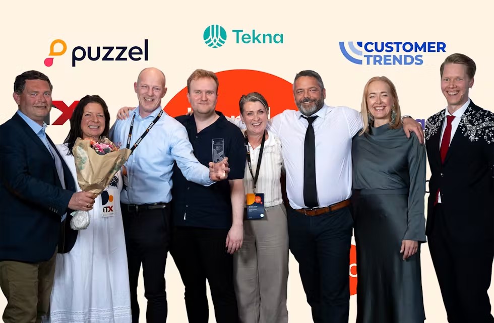 En gruppe smilende mennesker, med blomster og premie i glass. Foto.