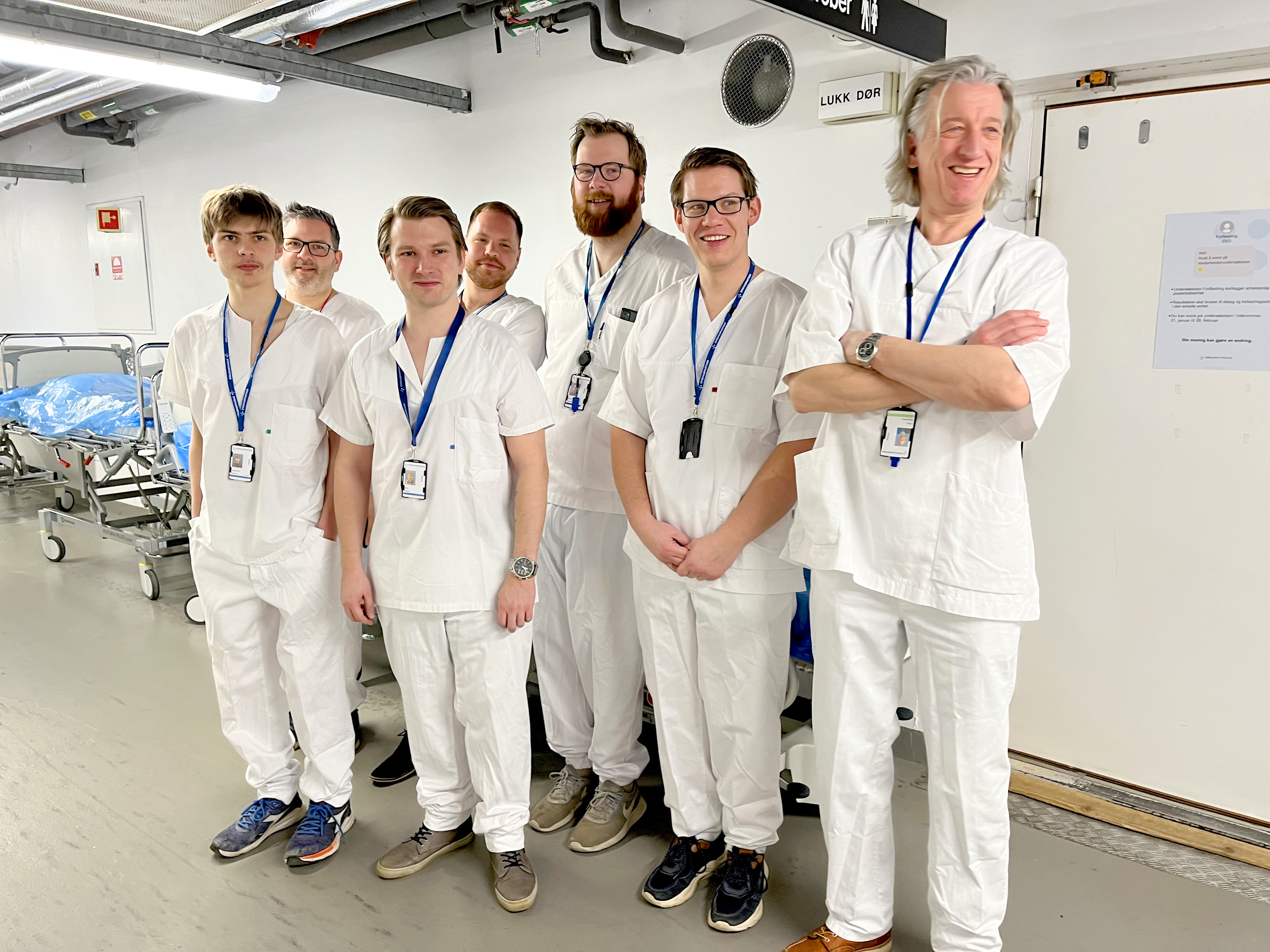 En gruppe menn i hvite sykehusklær poserer for et bilde i en sykehusgang. Foto.