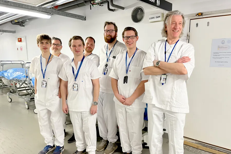 En gruppe menn i hvite sykehusklær poserer for et bilde i en sykehusgang. Foto.