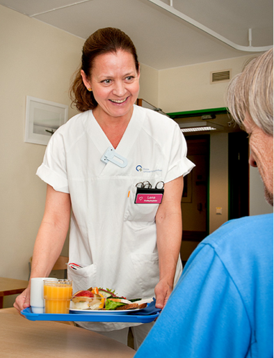 Sykepleier serverer mat til en pasient. Foto.