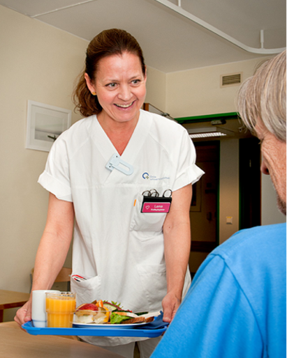 Sykepleier serverer mat til en pasient. Foto.