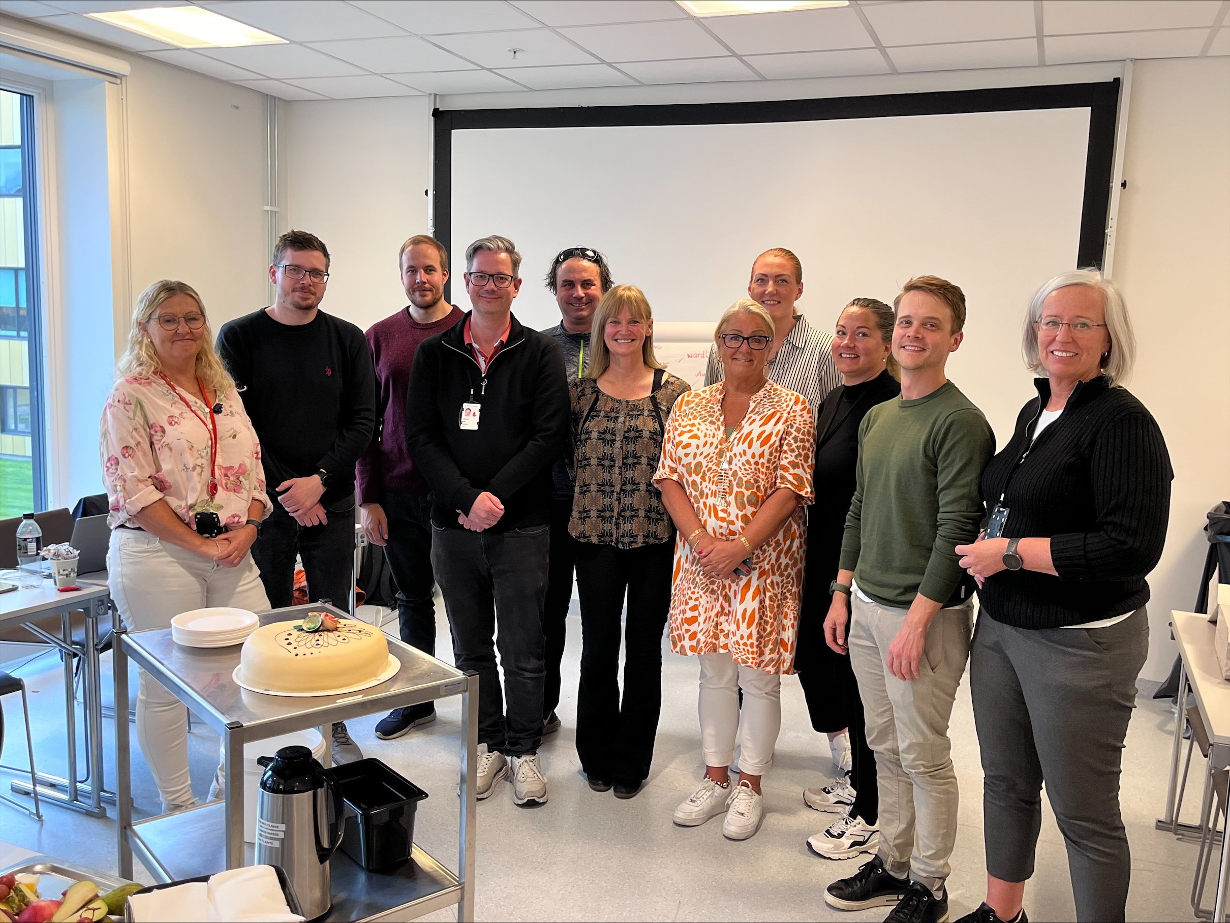 En gruppe mennesker som står foran en kake. Foto.