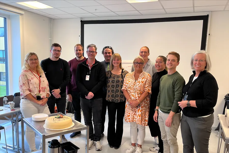 En gruppe mennesker som står foran en kake. Foto.