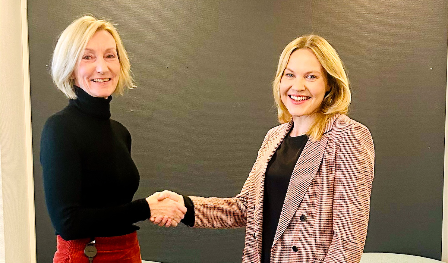 To damer smiler og tar hverandre i hånden. Foto.