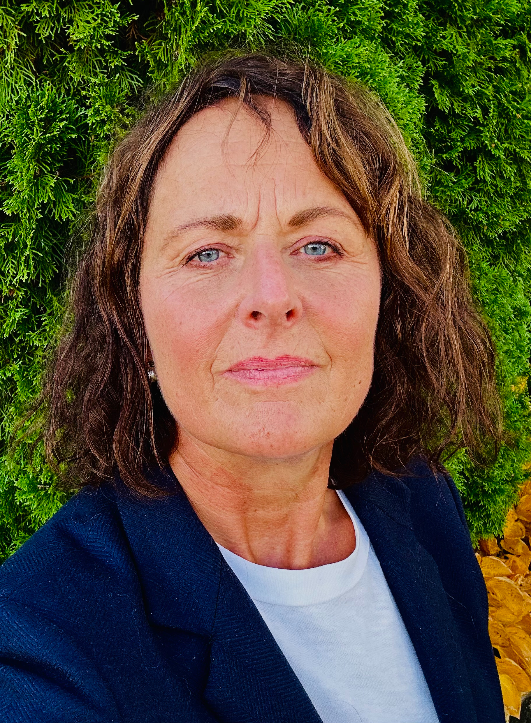 Dame med brunt hår og dressjakke. Foto.