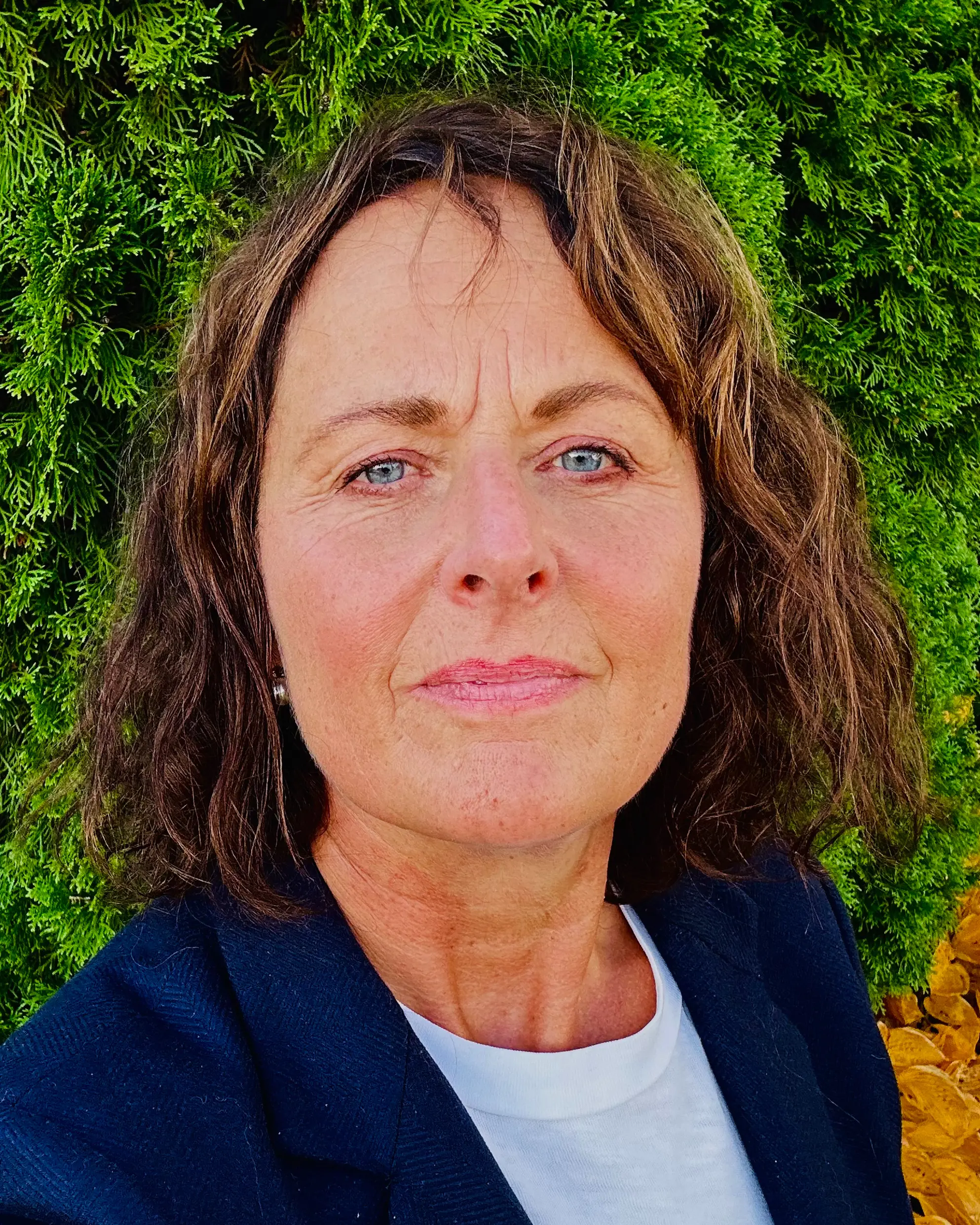 Dame med brunt hår og dressjakke. Foto.