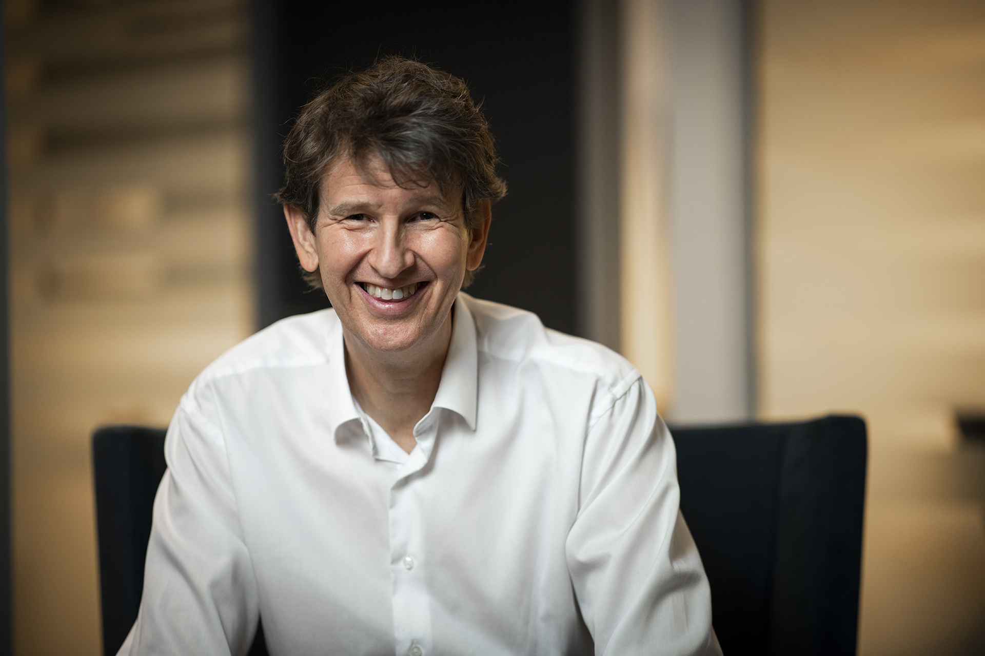 Smilende mann med mørkt hår og hvit skjorte.