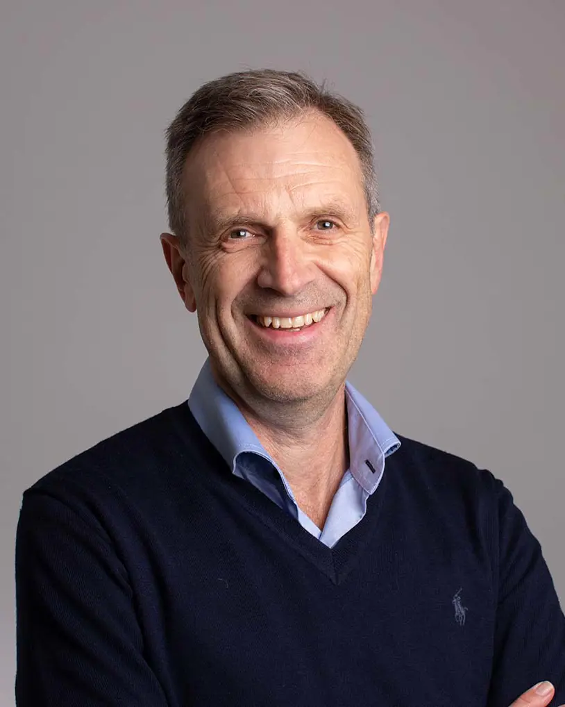 Smilende mann med grått hår, skjorte og genser. Foto.